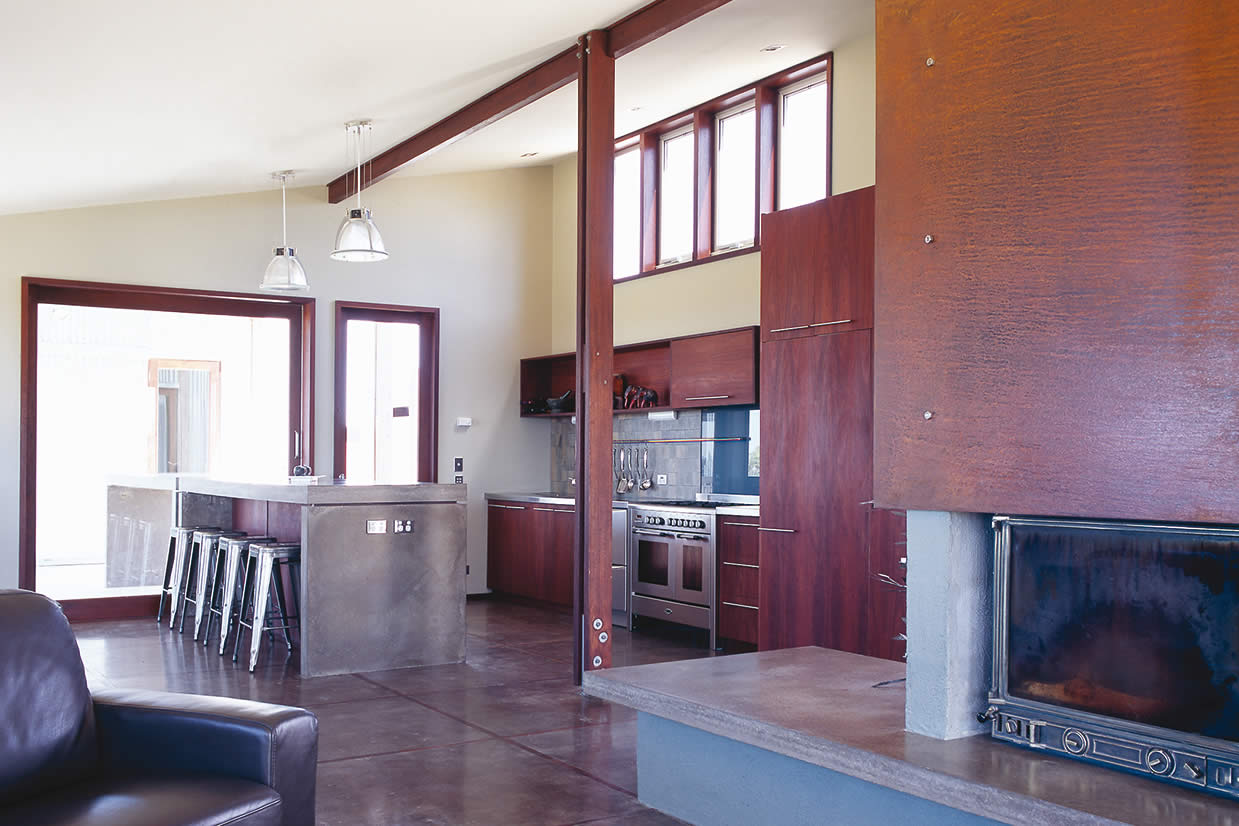 House Byrne, South Gippsland, Victoria: Interior finishes to the living / dining / kitchen include concrete bench and floors with timber insets, a feature rusted steel fire panel and recycled hardwood timber doors and windows. Photo by Richard Gange.