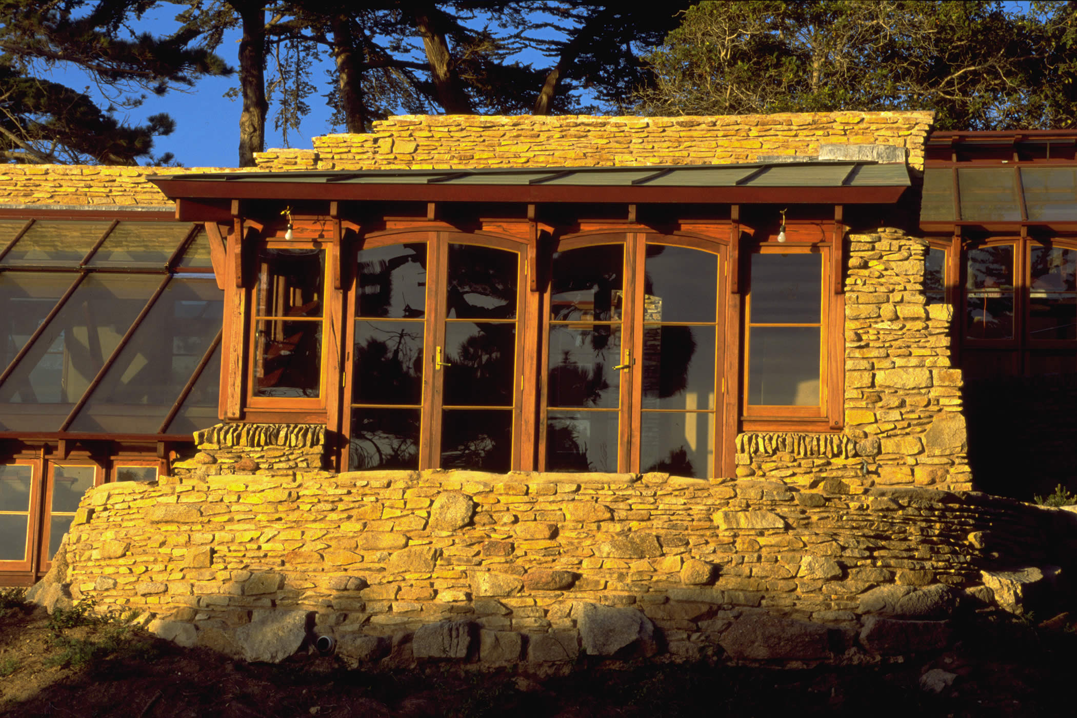 The James House Greenhouse, Carmel Highlands, California: Greenhouse detail of stonework and mixed eucalyptus hardwood recycled timber doors which interpret Charles Greene’s James House main house Mission Revival Style. Photo by James Morrison.