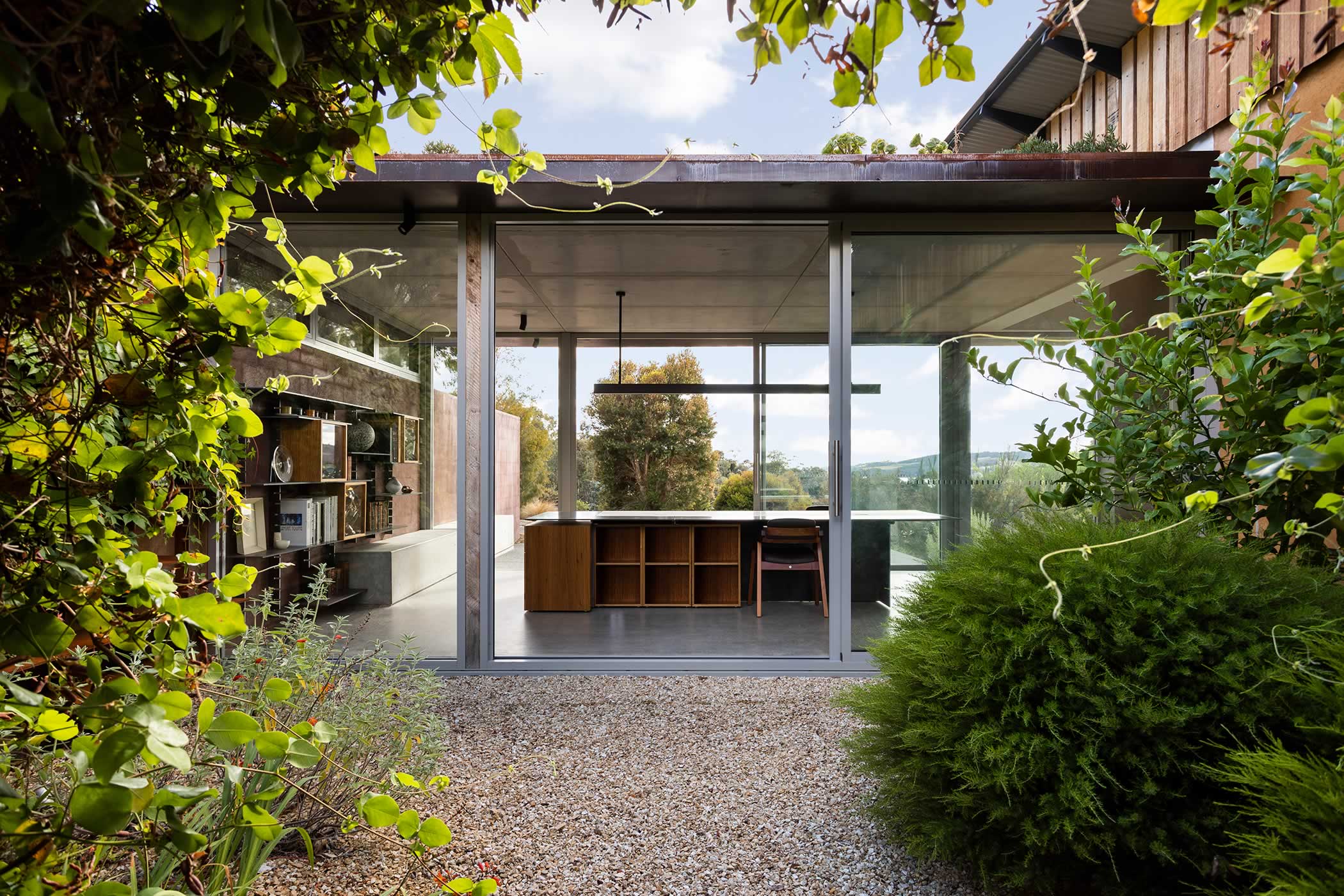Residential extension, Kettering, Tasmania: The studio extends into the existing lush sunken courtyard-garden, immersed in a world of intimacy and calm. Continuous garden wall steel shelving and concrete seating blur the boundaries. Photo by Adam Gibson.