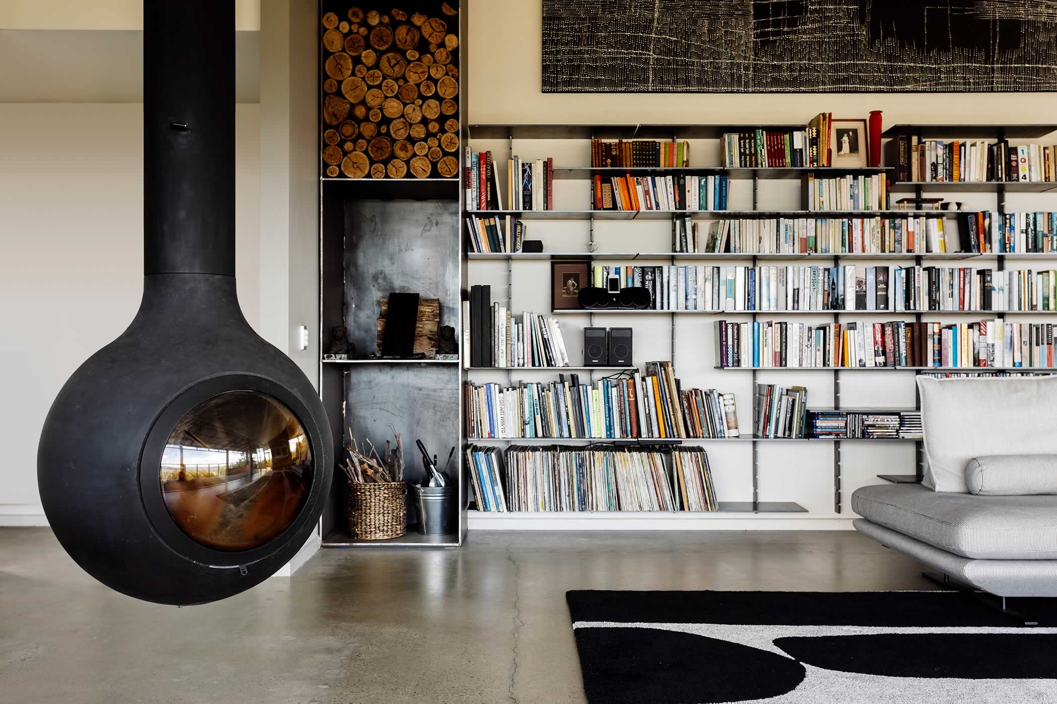 Residential extension, Kettering, Tasmania: A beautiful orb-shaped hanging wood-fire provides winter warmth and sculptural interest. Bespoke steel shelving houses books and collectables that further personalise the living room. Photo by Adam Gibson.