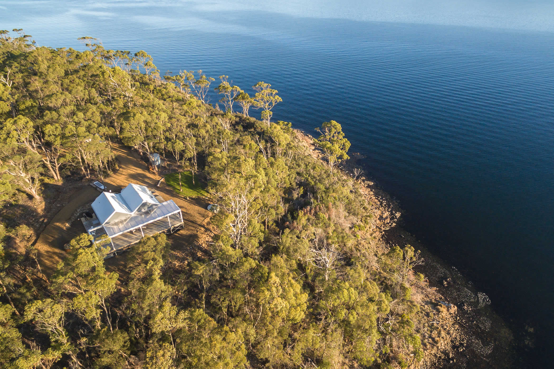 The Boat House, Blubber Head, Tasmania: An aerial view shows the remote luxury Boat House accommodation set on a private peninsula in forest acreage surrounded by sea, with walking access to the nearby water’s edge. Photo by Open2View.